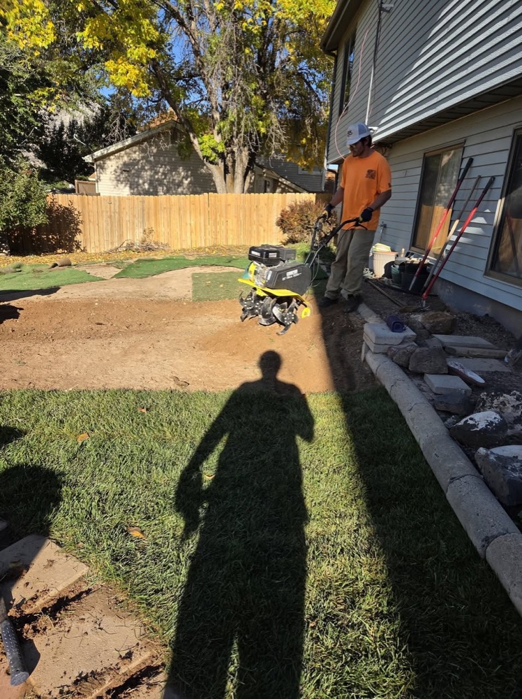 A Dude and a Mower crew member in an orange shirt working a backyard with a walk-behind machine