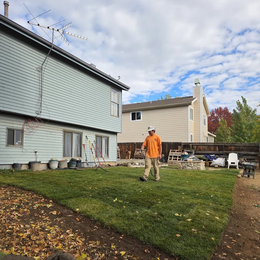 A crew member in an orange shirt walking across a freshly finished lawn, with fallen leaves in the foreground