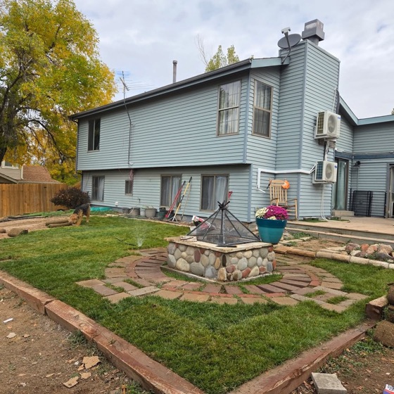 A tidy finished lawn, stone fire pit and a planter of flowers in front of a two-story house